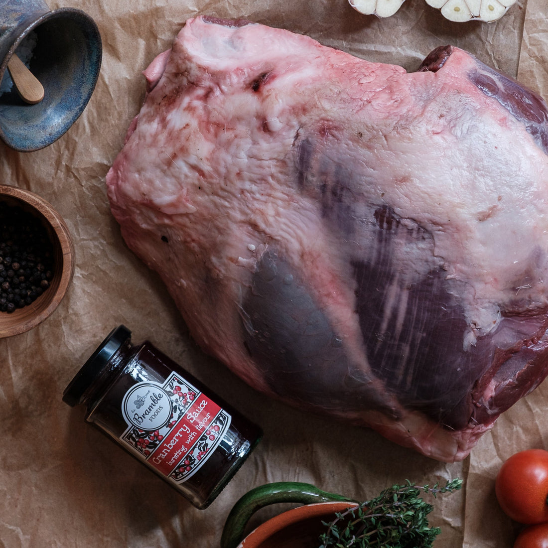 Raw venison haunch with spices, tomatoes, and herbs on brown paper