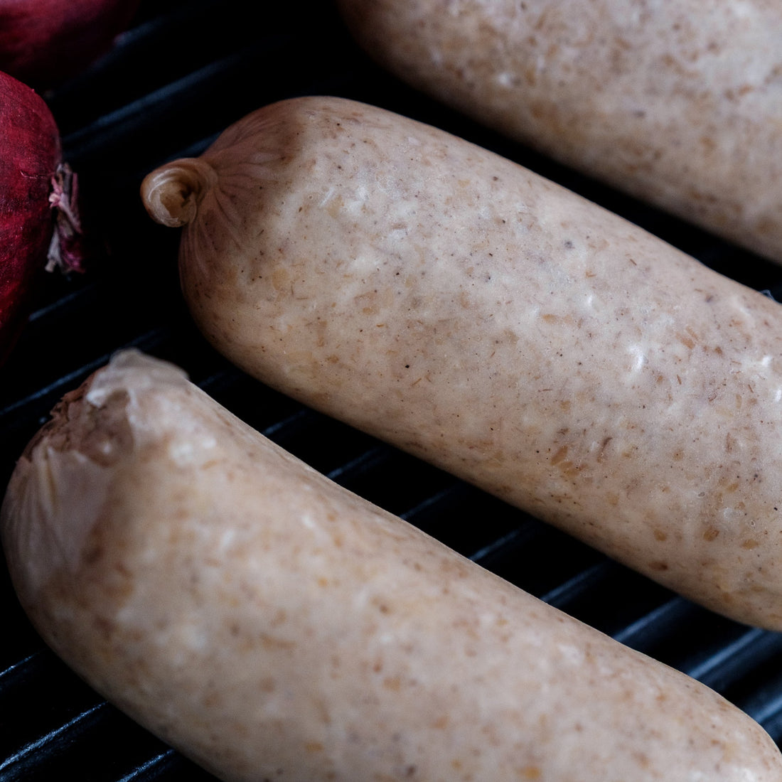 Three white puddings on a grill with a red onion in the background