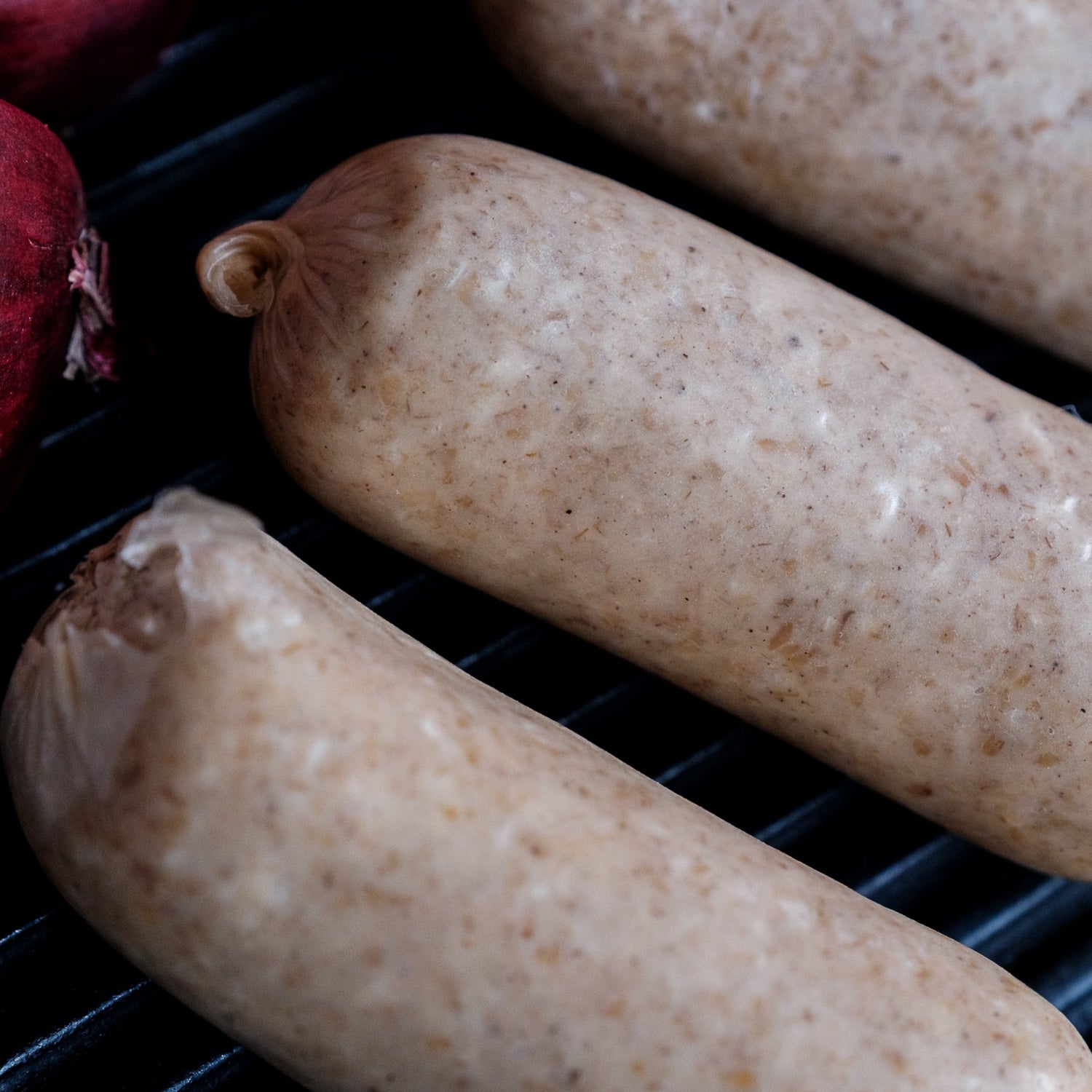 Three white puddings on a grill with a red onion in the background