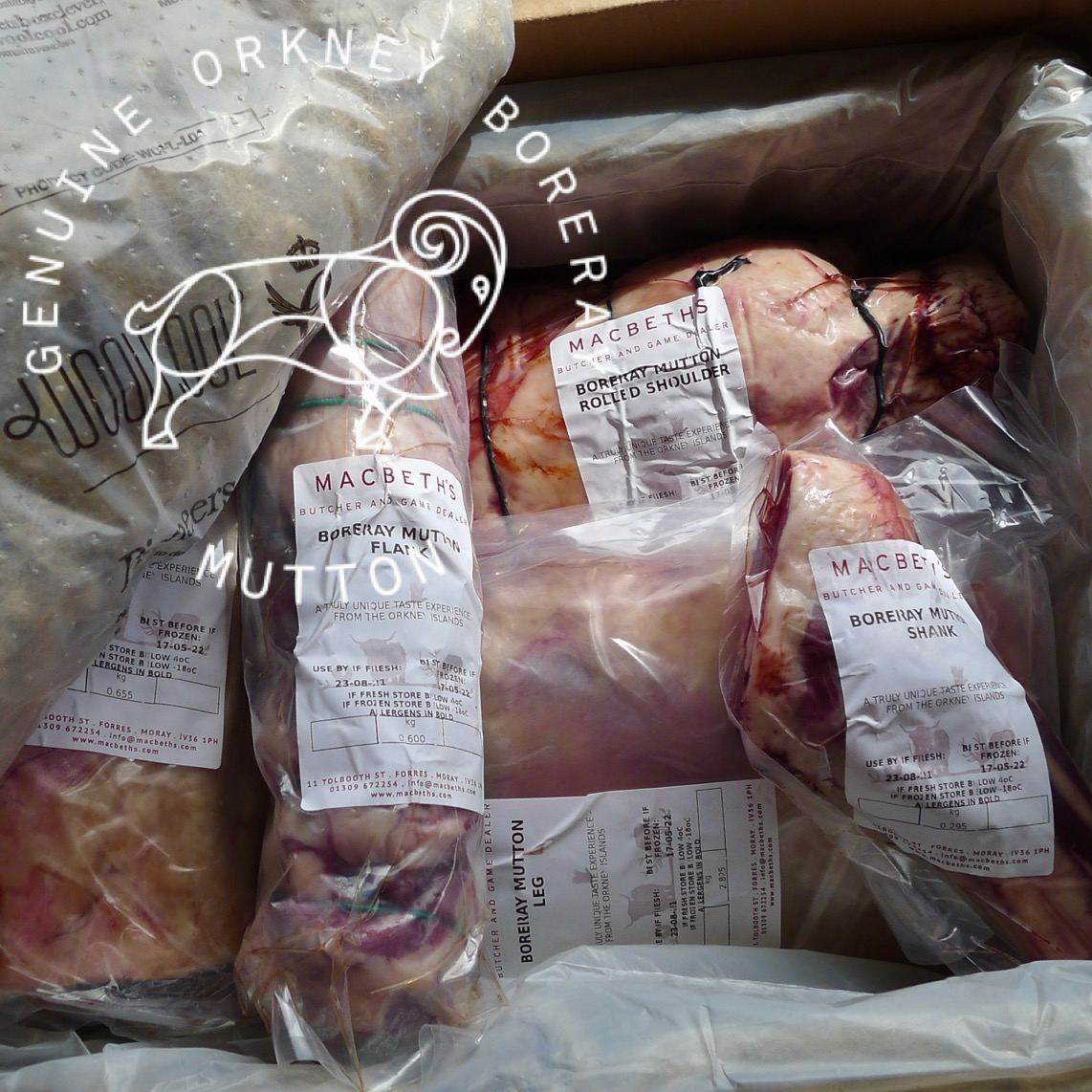 Raw mutton cuts packaged in clear plastic bags with white labels, arranged inside a cardboard box. The packaging has a circular logo and text reading &